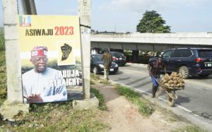 A vendor carries yams in wheelbarrow as he walks past a campaign poster of presidential candidate of the ruling Action Progressives Congress (APC) Bola Tinubu, displayed ahead of political campaigns in Lagos, on September 20, 2022. afp.com - Pius Utomi EKPEI